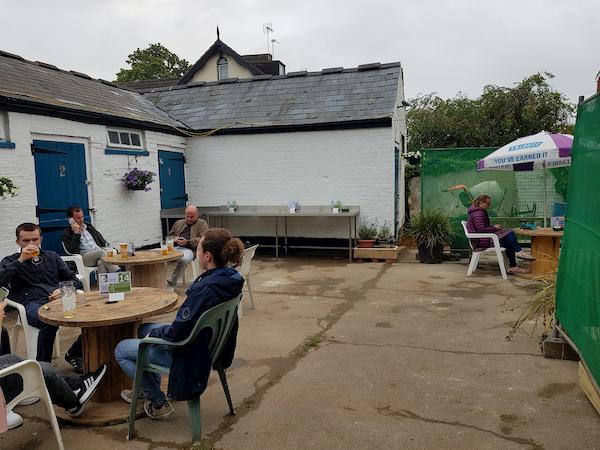 White stables in background, folk sitting at benchseat in the foreground