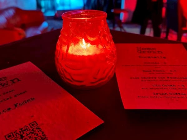Red candle on a table inside The Coach House along with the special drinks and music menues.