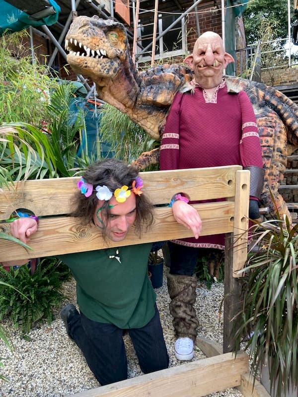 Harry oin the stocks with a dinosaur behind him