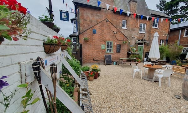 Wider pciture of The Courtyard showing lots of flowers on walls, down a ground level and on the pub. 