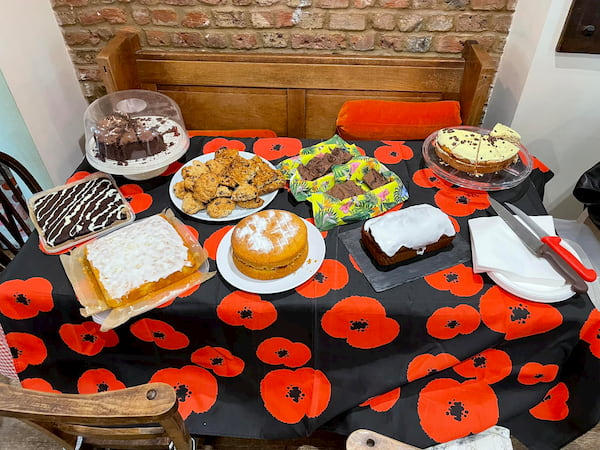 Table covered with a poppy themed tablecloth with lots of cakes on top