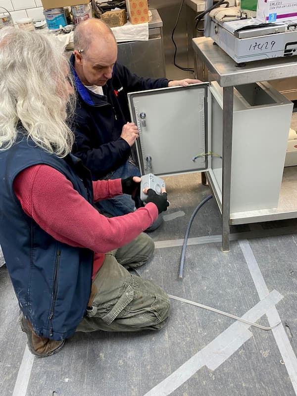 Keith and Tony working on the electric distribution box within The Kitchen