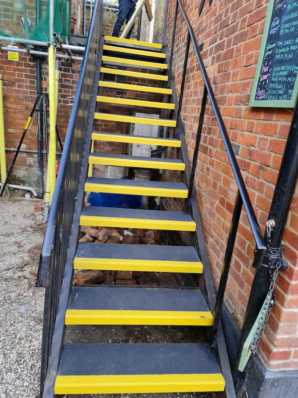 Metal stairs with new treds, yellow safety marking and a second rail at the side of The Coach House.