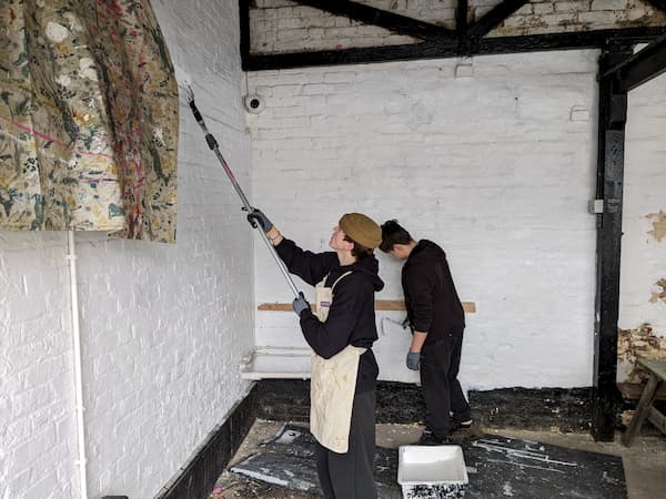 Students whitewashing the walls using long poles to reach up high.