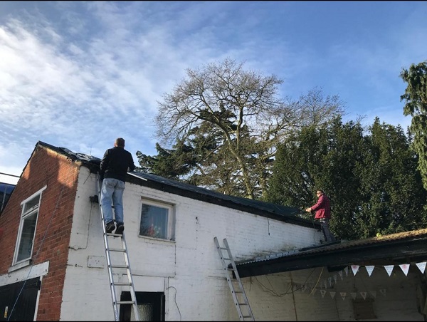 Lads on ladders fixing the tarpaulin on the Coach House roof