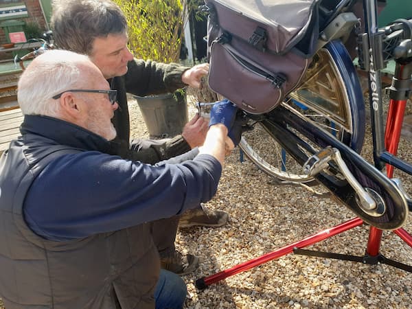 Two men - one the owner - working together to repair a bike.